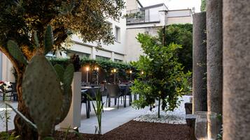 An outdoor patio area with tables and chairs, surrounded by plants and a cactus.