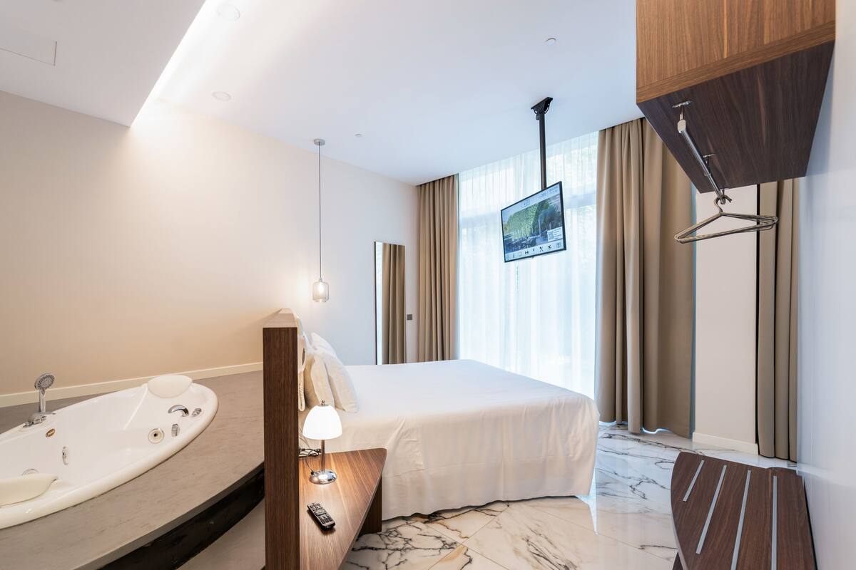 Una camera d'albergo moderna con un letto grande, una vasca da bagno integrata, un televisore a schermo piatto e un armadio in legno.