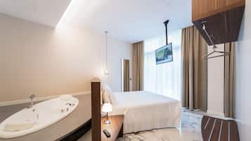 Quarto de hotel moderno com uma cama grande, banheira integrada, televisão de tela plana e um guarda-roupa de madeira.