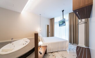 Een moderne hotelkamer met een groot bed, een inbouwbubbelbad, een flatscreen televisie en een houten garderobe.