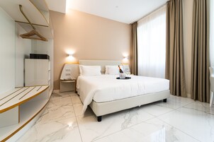 Een moderne hotelkamer met een groot bed, een nachtkastje met lamp, een kledingkast en een kapstok.