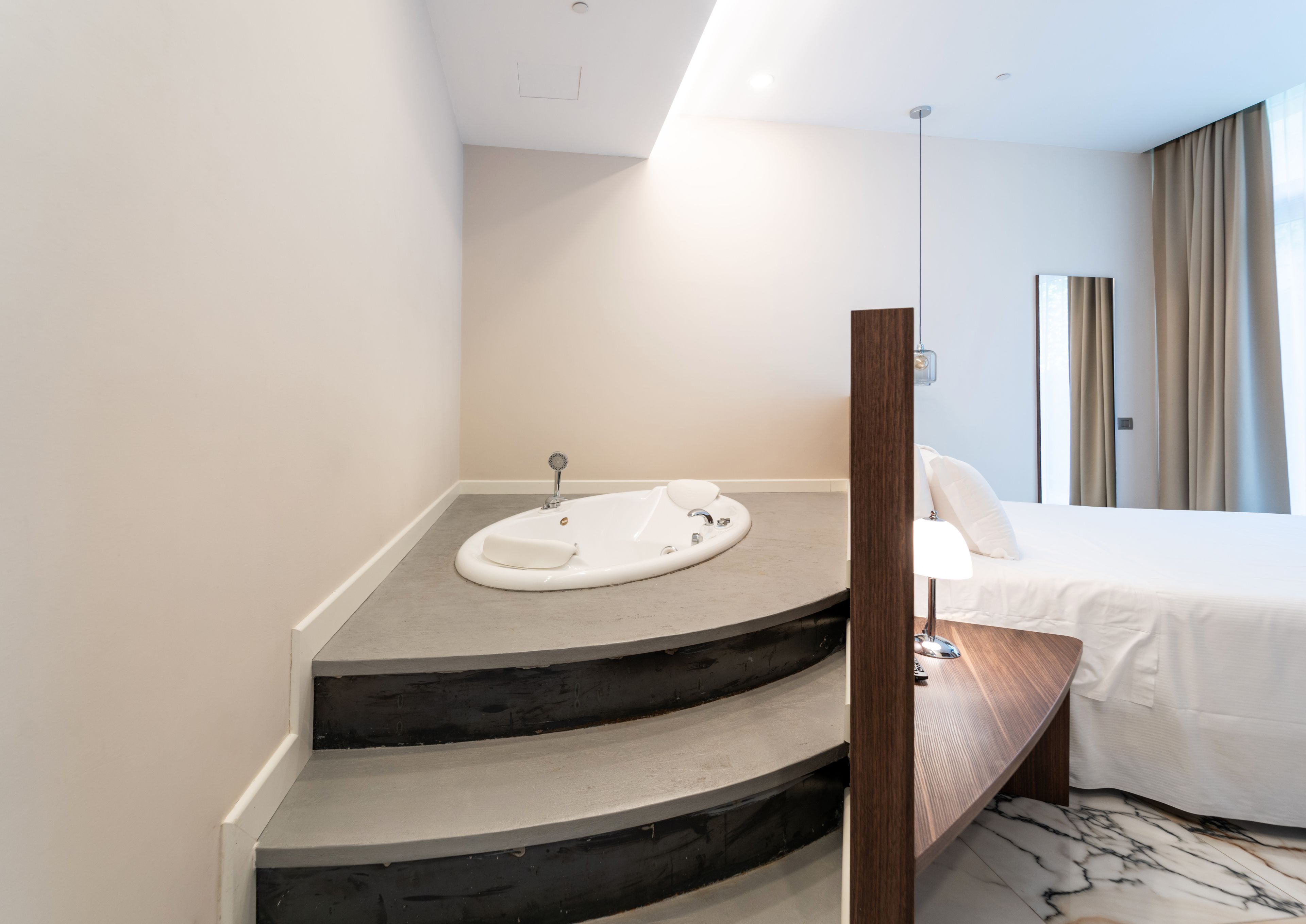 Un baño moderno con una bañera curva, un mueble de tocador de madera y una cama con ropa blanca.
