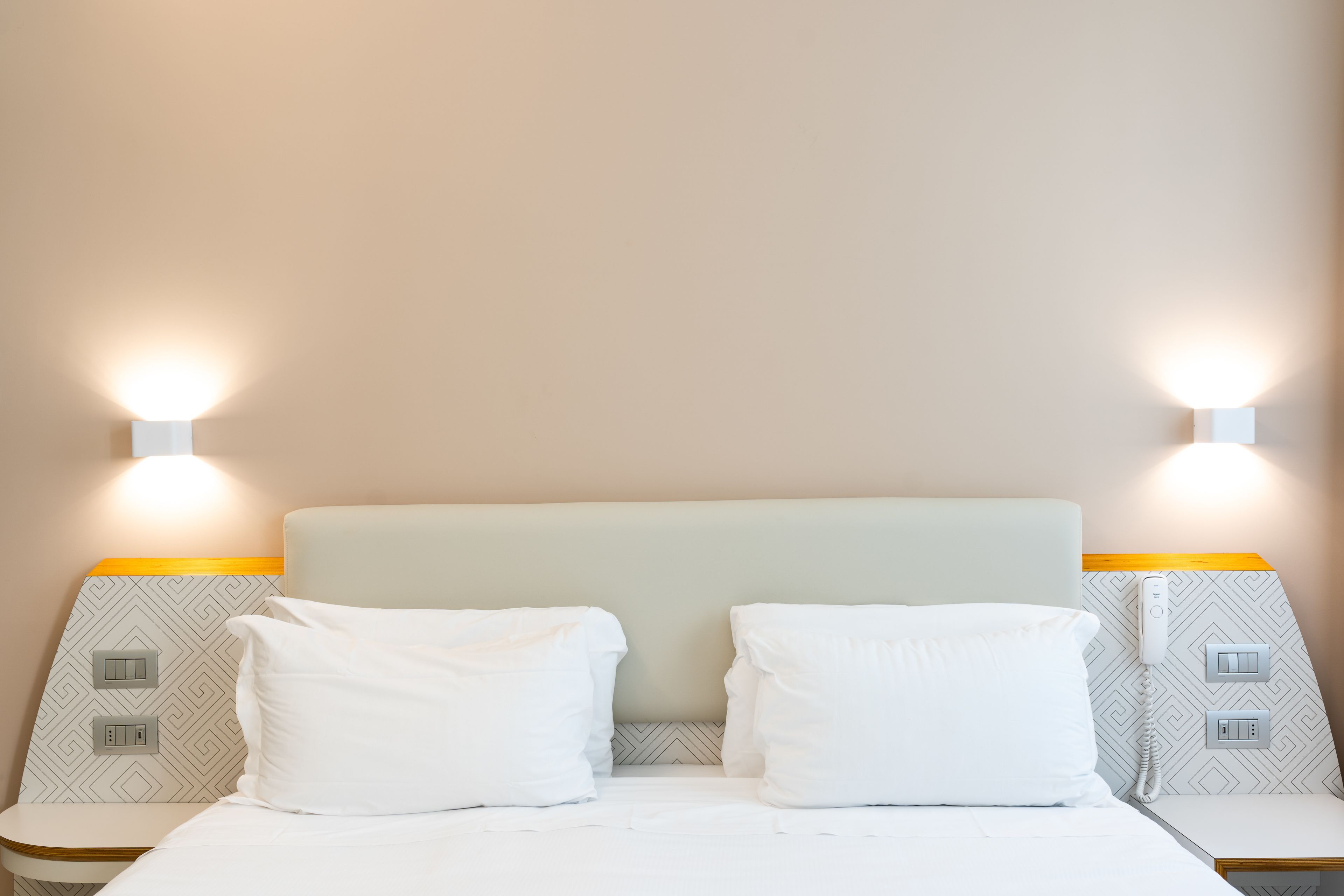 A hotel room with a bed, two bedside tables, and wall-mounted light fixtures.