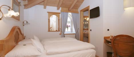 Un dormitorio con techo de madera, una cama con ropa de cama blanca, una mesita de noche de madera con un teléfono, una silla y una pequeña mesa con una lámpara.