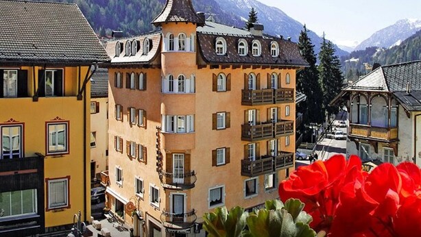 Un immeuble à plusieurs étages, doté d’une tour imposante, de balcons et offrant une vue sur les montagnes en arrière-plan.