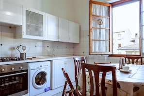 A kitchen with white cabinets, a washing machine, a stove, and a dining area with wooden chairs and a table.