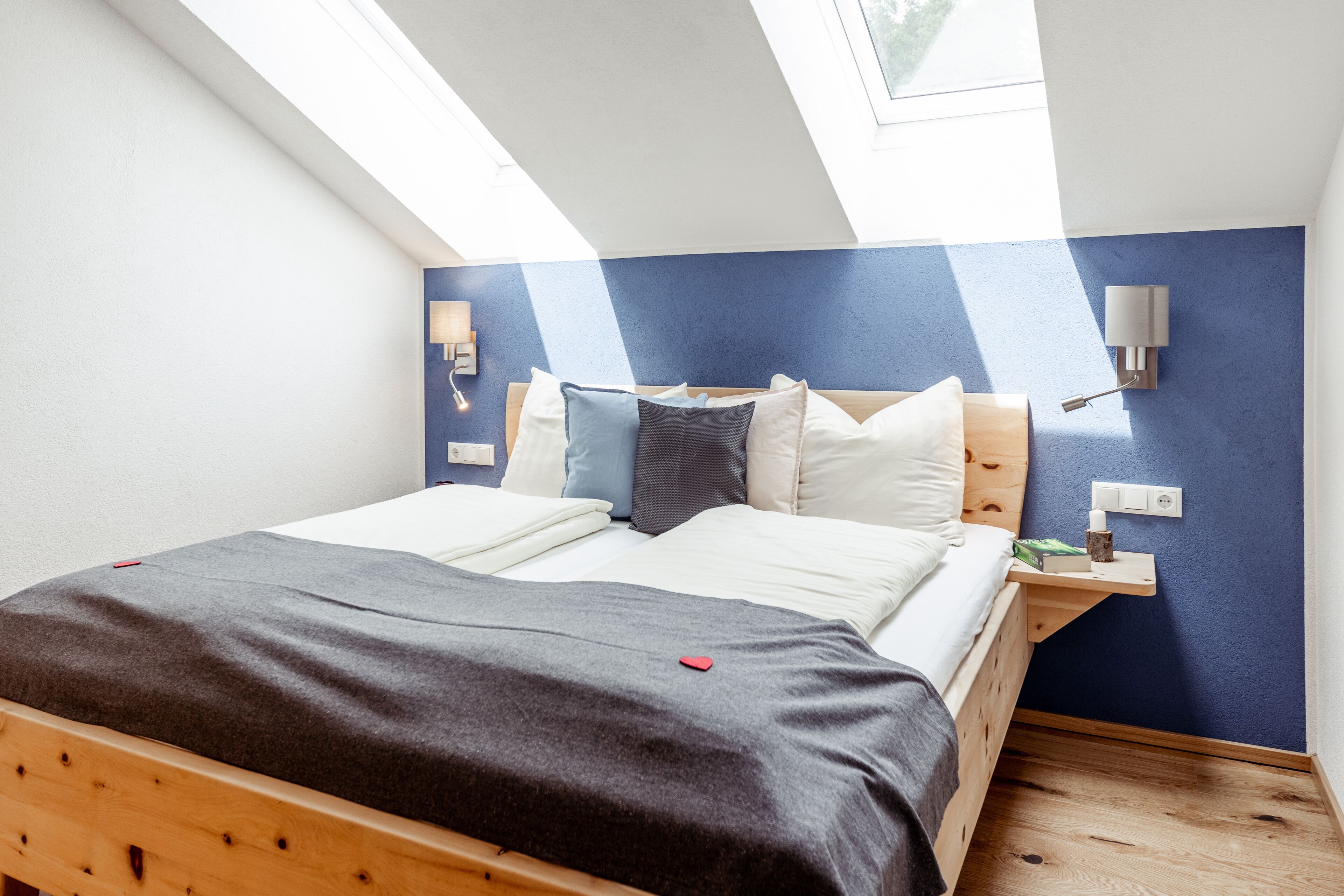 Una camera da letto con un lucernario, un letto con coperta grigia e un comodino con una lampada.