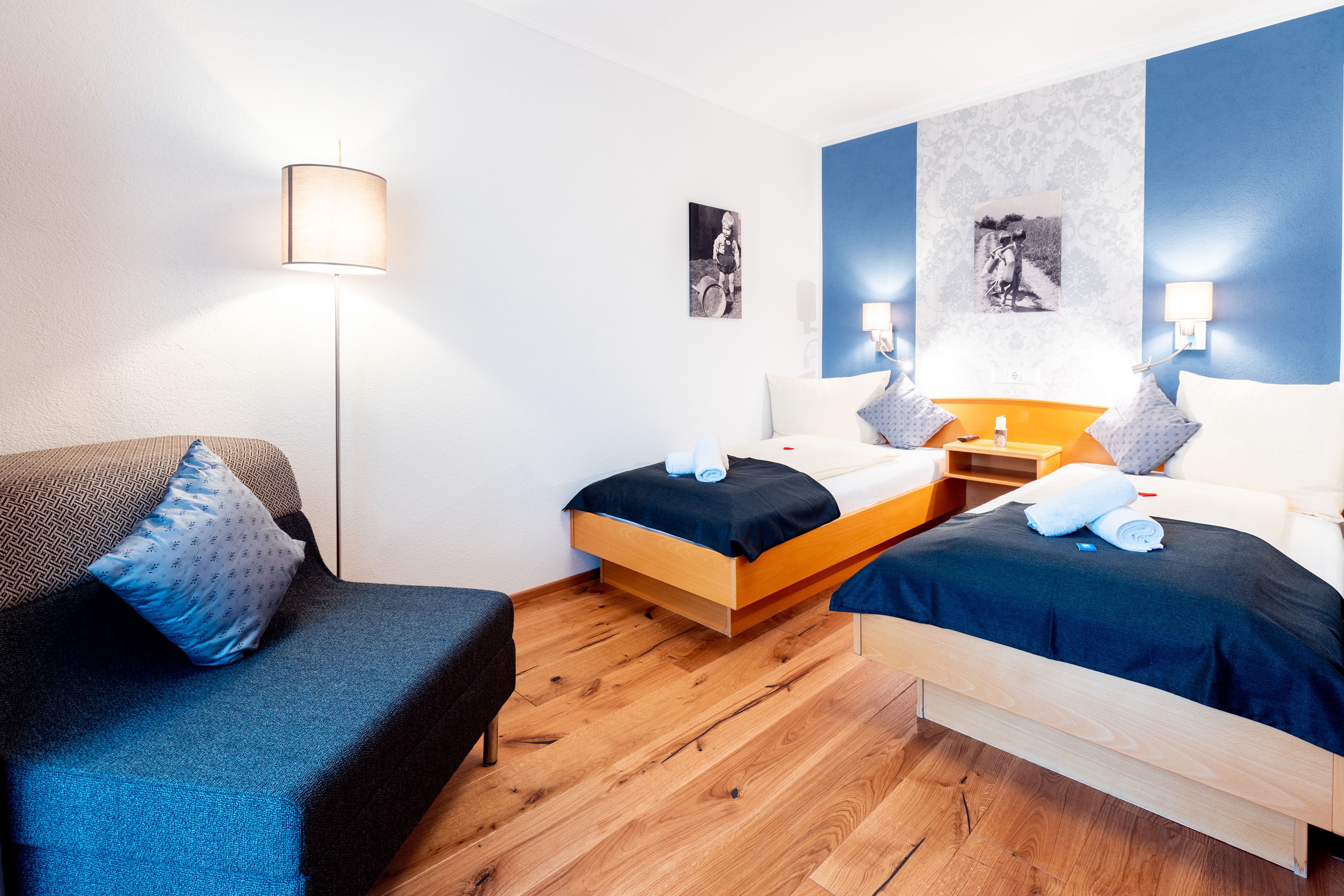 A hotel room with two beds, a sofa, a lamp, and artwork on the walls.