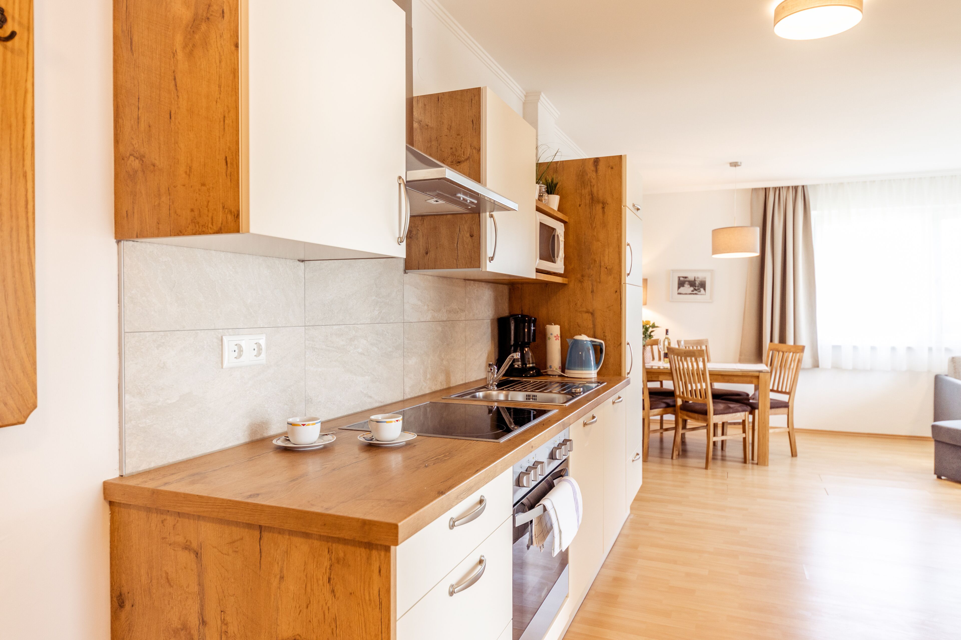 A modern kitchen with wooden cabinets, a built-in oven, and a dining area with a table and chairs.