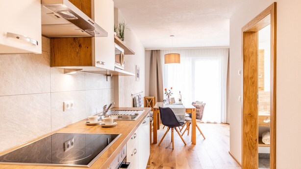 A modern kitchen with a built-in stove, wooden cabinets, and a dining area with a table and chairs. - Kärnten Apartment Turnersee (Sankt Kanzian am Klopeiner See)