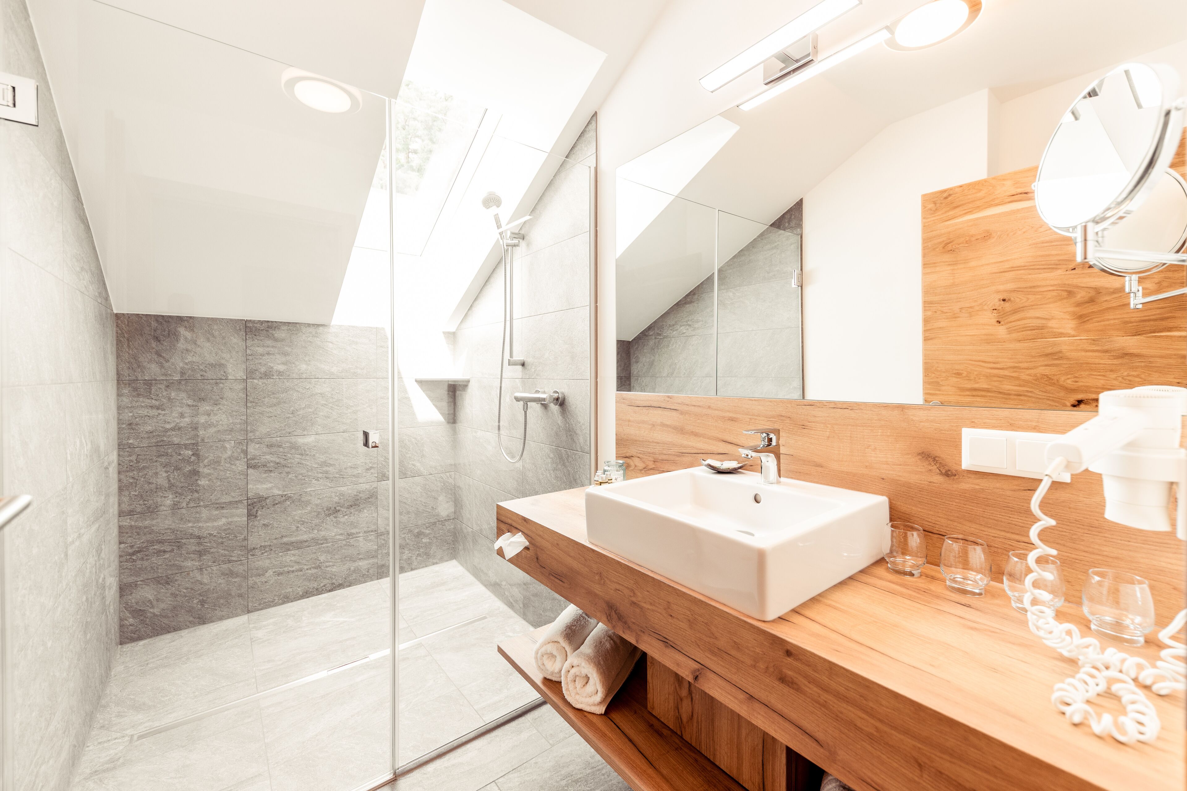 A modern bathroom with a glass shower enclosure, a wooden vanity with a sink, and a mirror.
