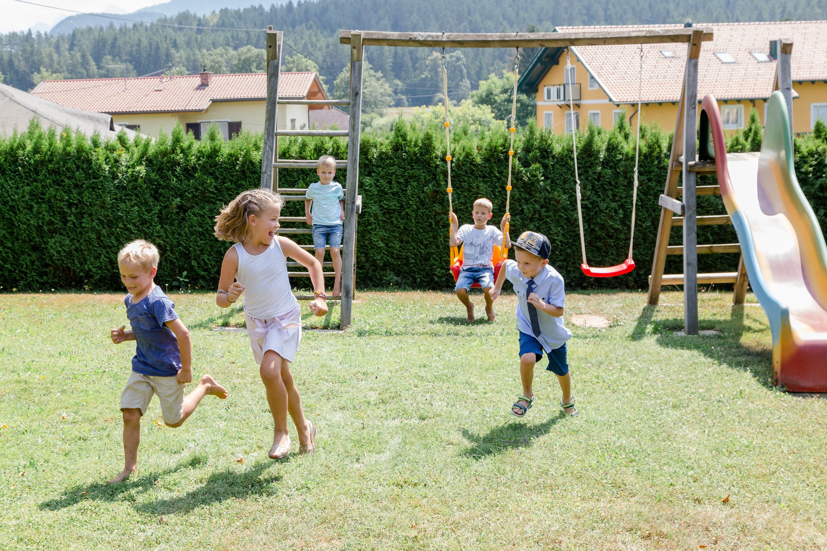 Un parque infantil con columpios y un tobogán, rodeado de césped y un seto.