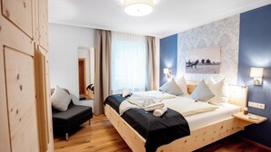 A bedroom with a wooden bed, a bedside table, a nightstand, a sofa, a mirror, and a window with curtains. - Kärnten Apartment Turnersee (Sankt Kanzian am Klopeiner See)