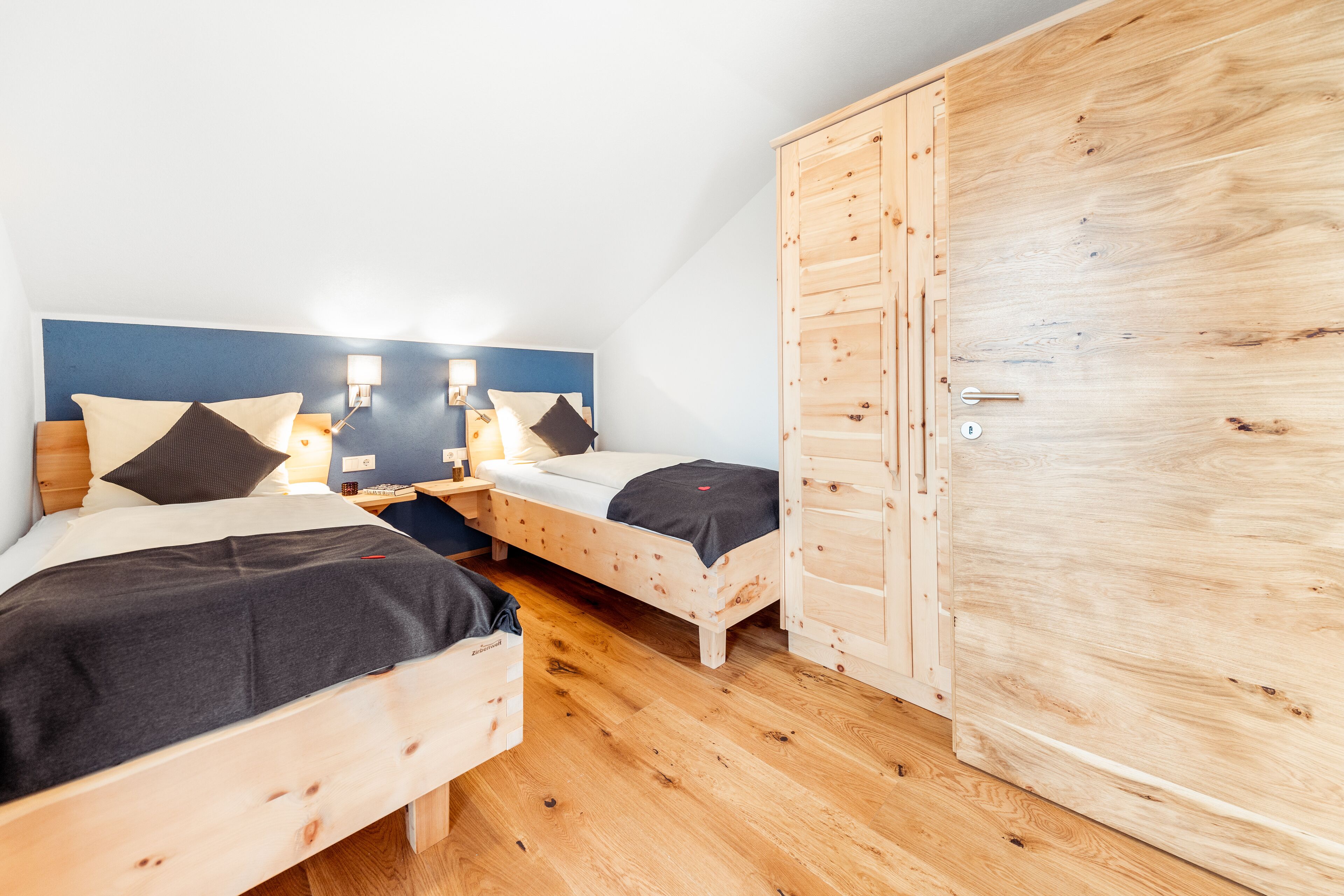 Un dormitorio con dos camas de madera, un armario y una mesita de noche con lámpara.