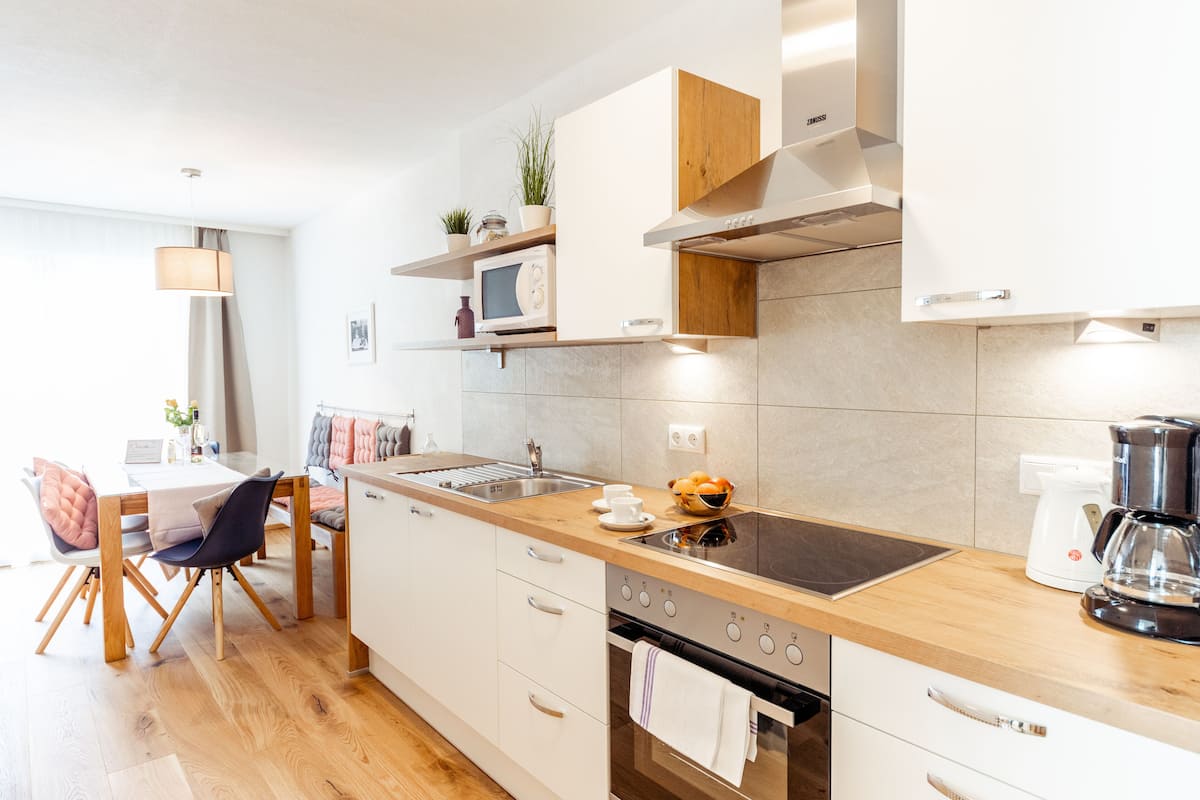 Une cuisine moderne avec des armoires blanches, un plan de travail en bois, un four à micro-ondes encastré, une cuisinière et une machine à café.