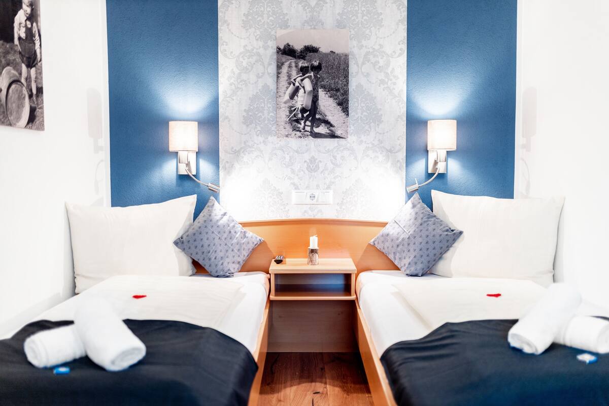Une chambre d’hôtel avec deux lits, une table de chevet avec une lampe, une photo encadrée accrochée au mur et une petite table placée entre les lits.