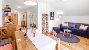 A modern living room with a wooden dining table, a sofa, and a coffee table. There are decorative items on the table and a plant in the corner. - Kärnten Apartment Turnersee (Sankt Kanzian am Klopeiner See)