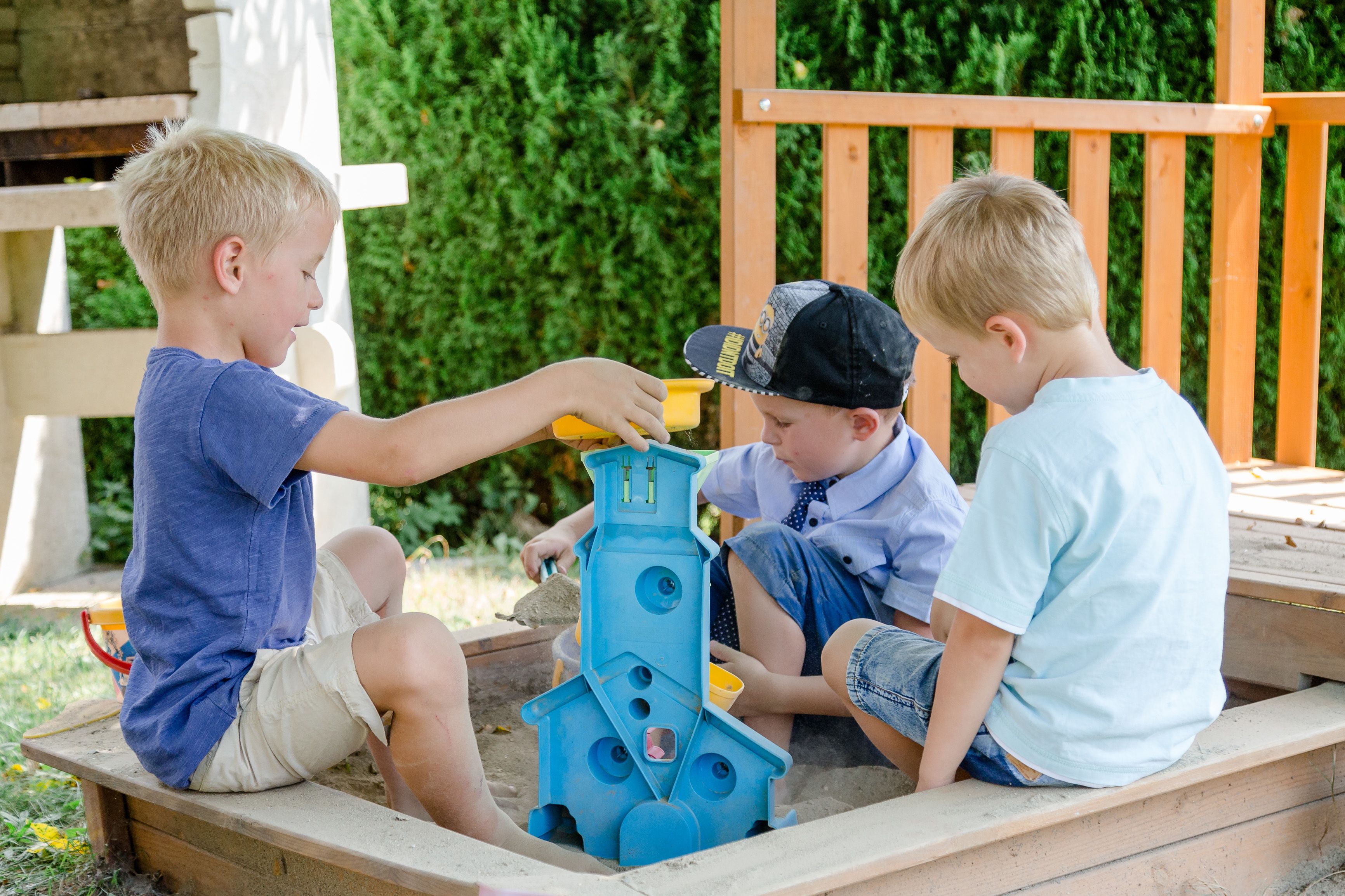 Tres niños jugando con una estructura de arena azul al aire libre.
