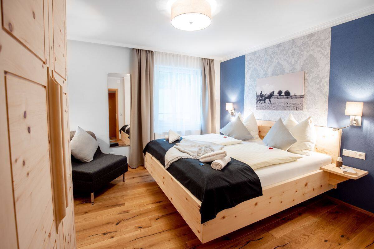 Une chambre d’hôtel moderne avec un lit en bois, un canapé et une grande fenêtre avec des rideaux.