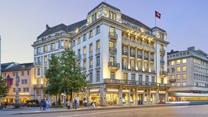 A large, historic hotel with multiple floors, a prominent flag, and a well-lit facade. - Mandarin Oriental Savoy, Zurich (Zürich)