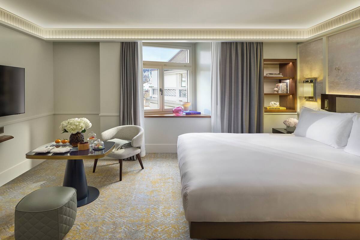A hotel room with a large bed, a desk with a chair, a television, and a window with curtains.