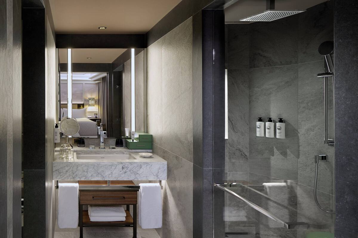 A modern bathroom with a marble sink, a glass-enclosed shower, and a wooden bench.