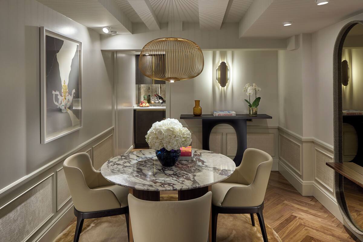 A dining area with a marble table, four chairs, a vase of flowers, and a pendant light.