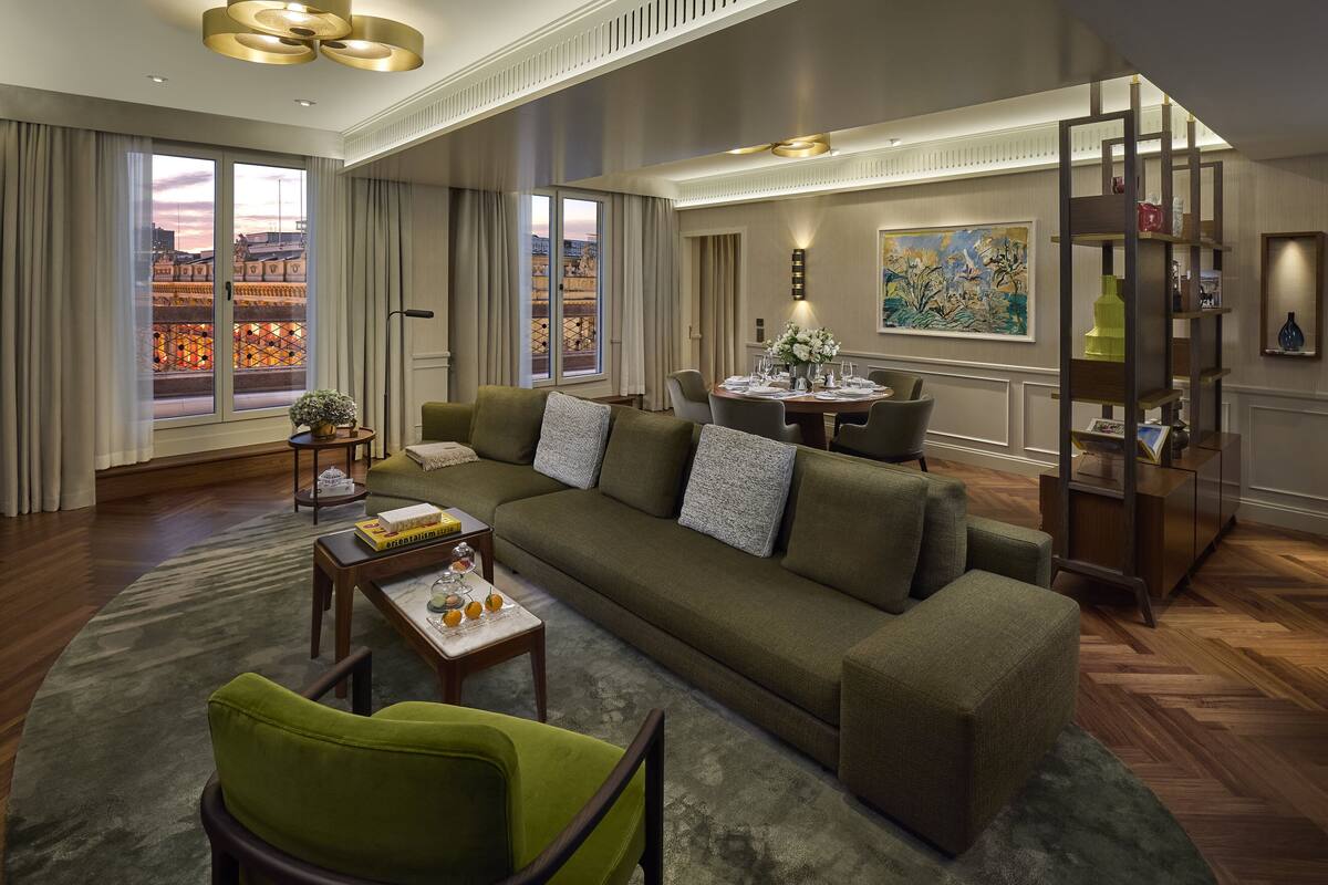 A modern living room with a large sofa, a coffee table, and a dining area with a chandelier.