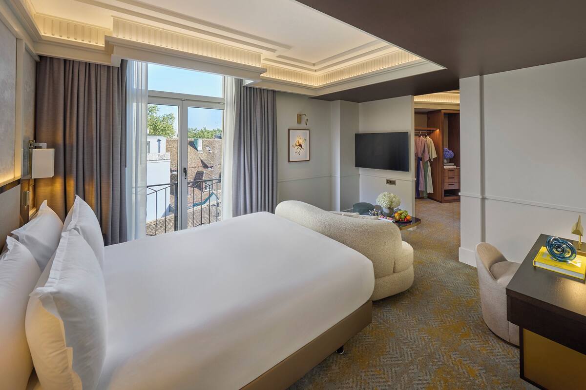 A hotel room with a large bed, a seating area, a TV, and a view of the outdoors.