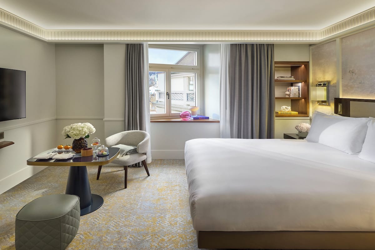 A hotel room with a large bed, a desk with a chair, a television, and a window with curtains.