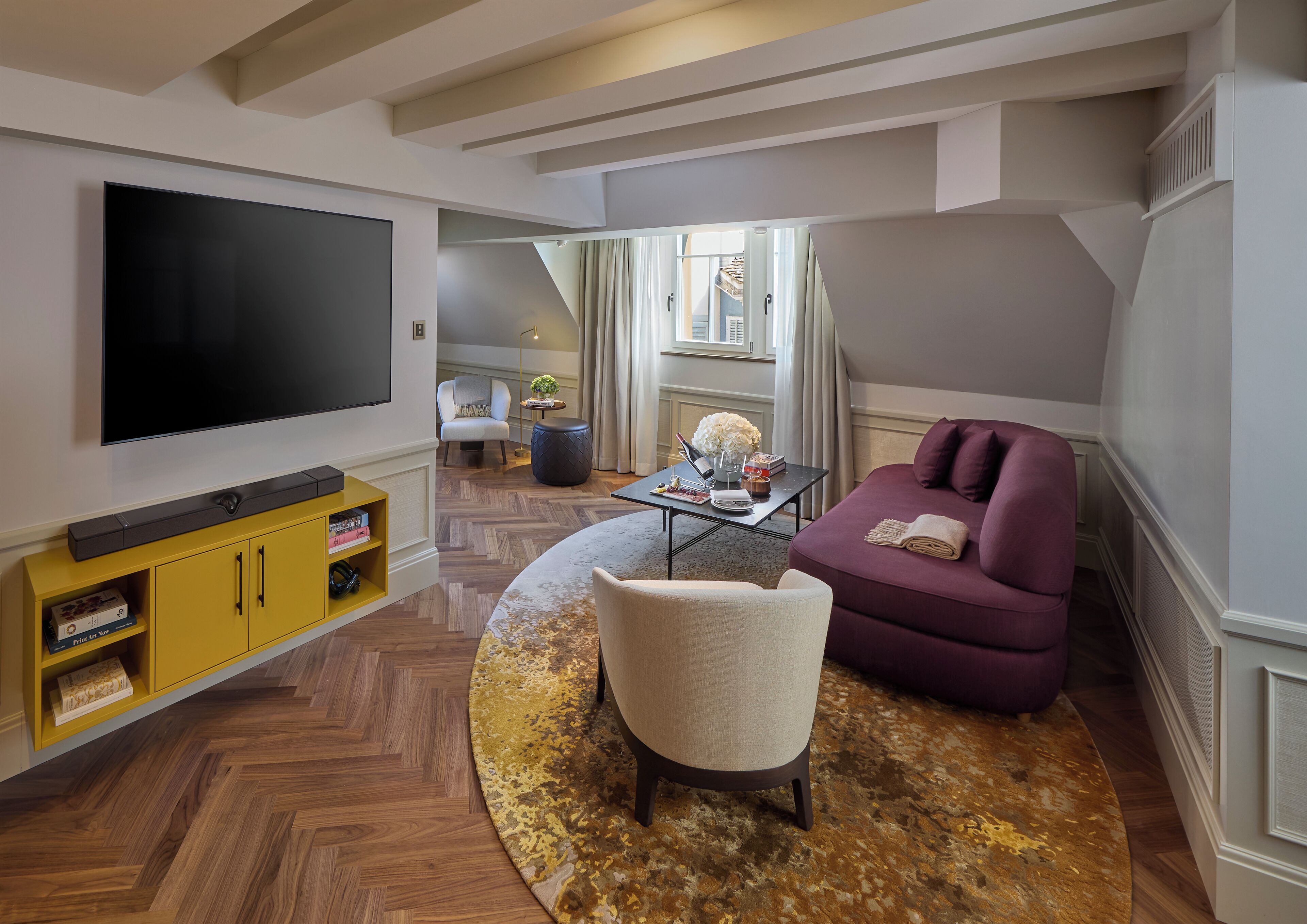 A modern living room with a flat-screen TV, a yellow entertainment unit, a purple sofa, a round coffee table, and a patterned rug.