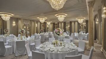 Un salón de banquetes con mesas redondas dispuestas para cenar, grandes candelabros y elegantes centros de mesa con flores.
