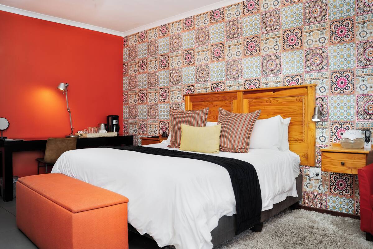 Una habitación de hotel con una cama grande, un escritorio, una silla y una pared roja.