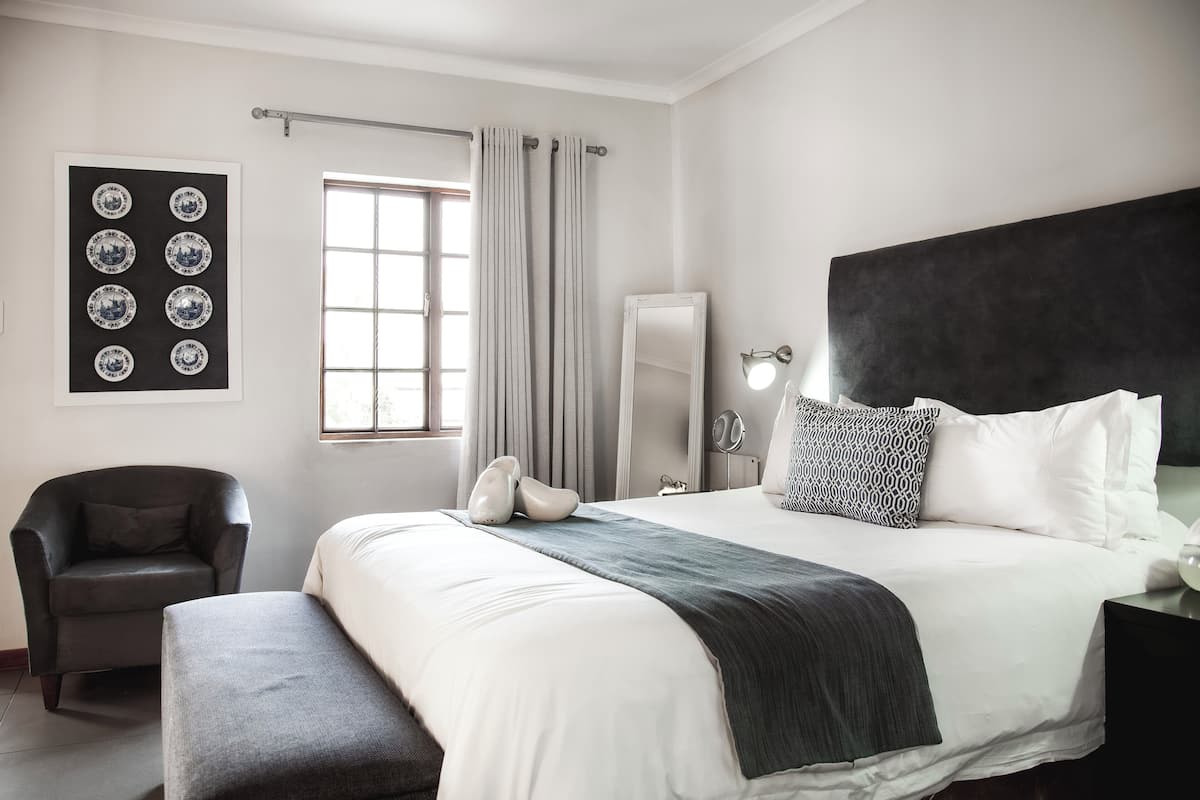 Un dormitorio moderno con una cama grande, una silla, un banco, un espejo y una lámpara de pared.