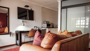 A modern living room with a leather sofa, a flat-screen TV, a coffee machine, and a dining area. - Yalla Yalla Boutique Hotel (Emalahleni)