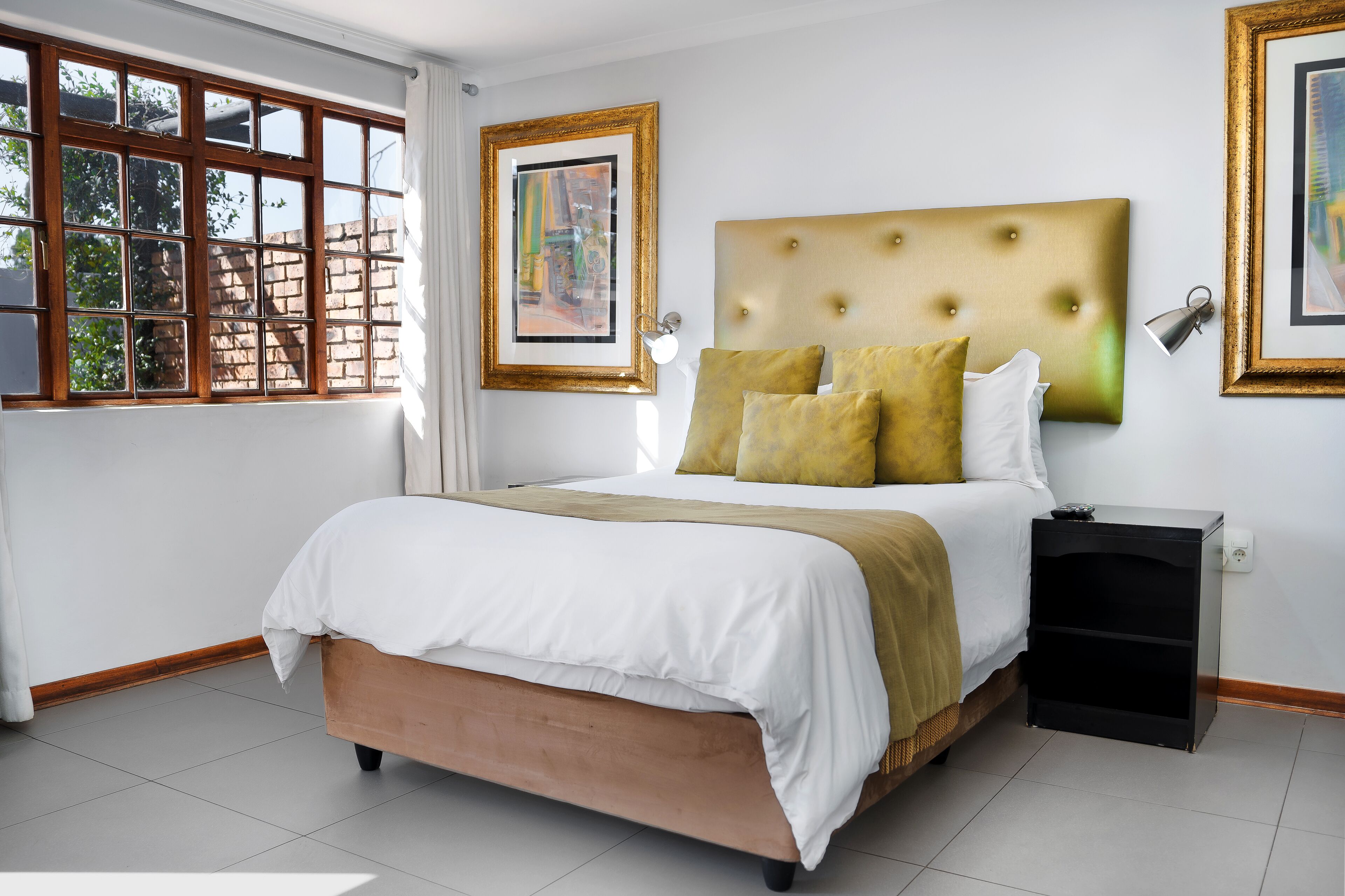 A neatly made bed with a headboard, a bedside table, and a window with a view of trees.