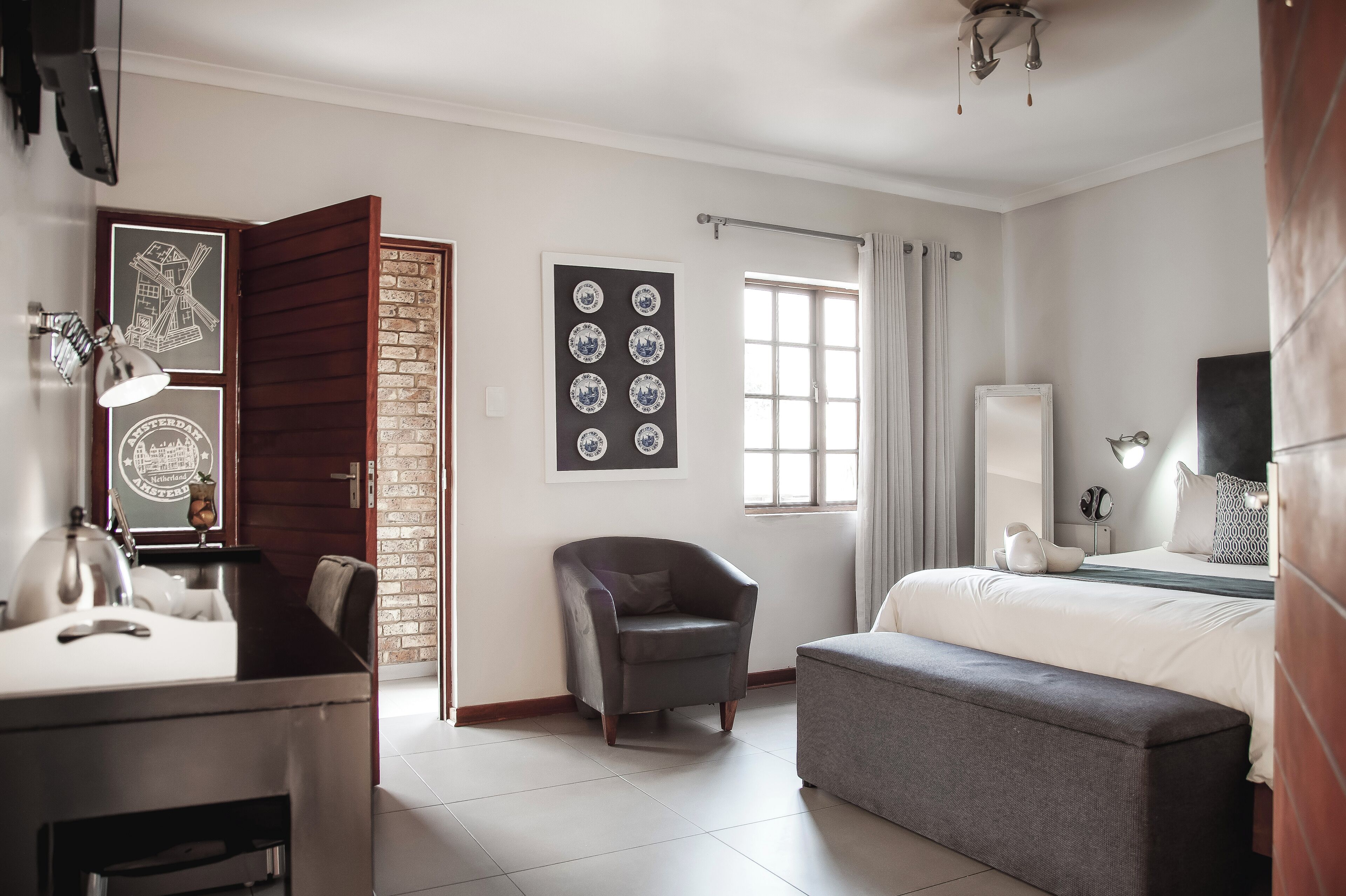 A modern hotel room with a bed, a desk, a chair, a bench, a window, and artwork on the walls.