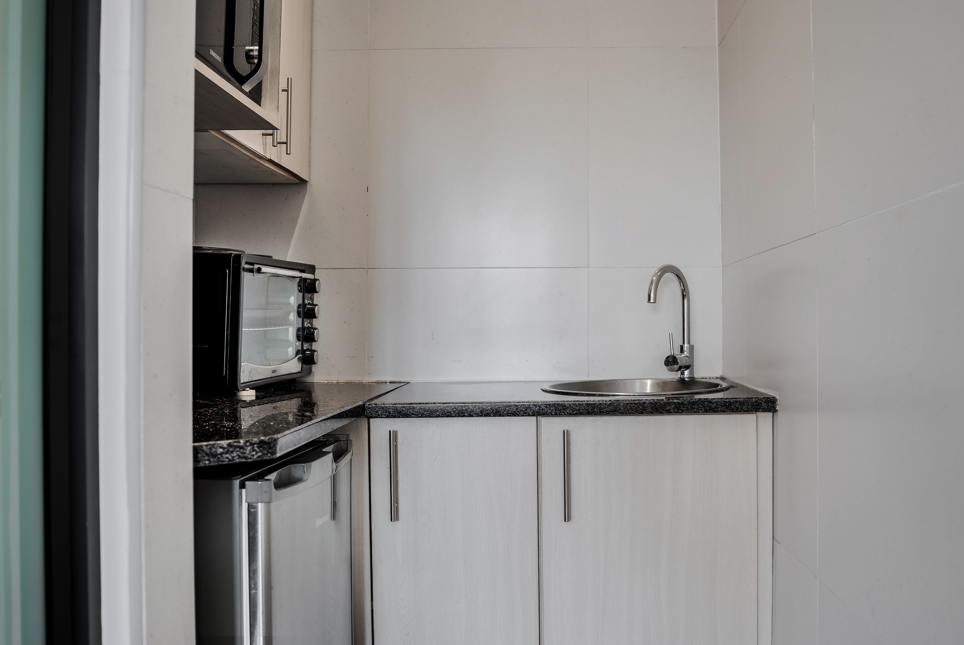 A compact kitchen with white cabinets, a stainless steel sink, and a microwave.