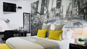 A hotel room with a large bed, a desk, a chair, a TV, and a cityscape mural on the wall. - Yalla Yalla Boutique Hotel (Emalahleni)