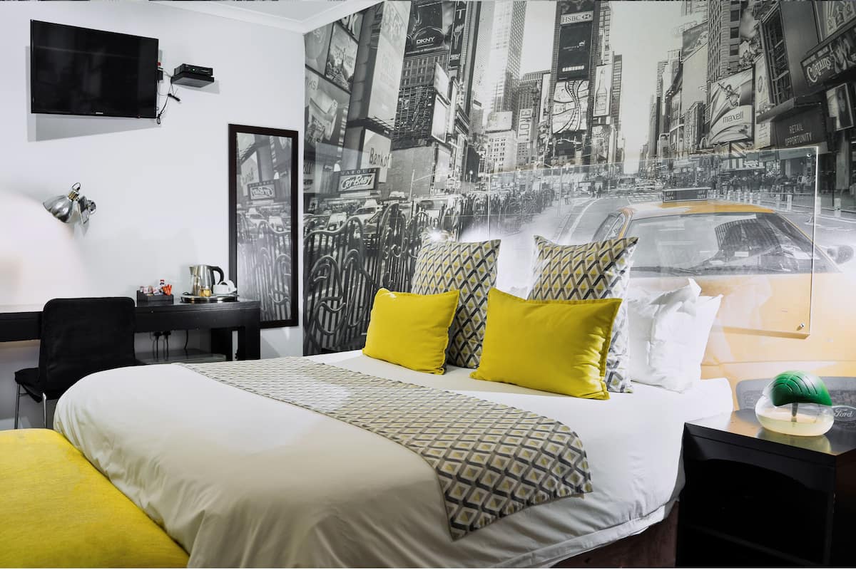 Habitación de hotel con una cama grande, un escritorio, una silla, un televisor y un mural con vista a la ciudad en la pared.