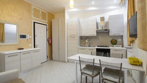 A modern kitchen with white cabinets, a dining table with chairs, and a yellow bag on the table. - Gold Vatican Apartment (Rome)