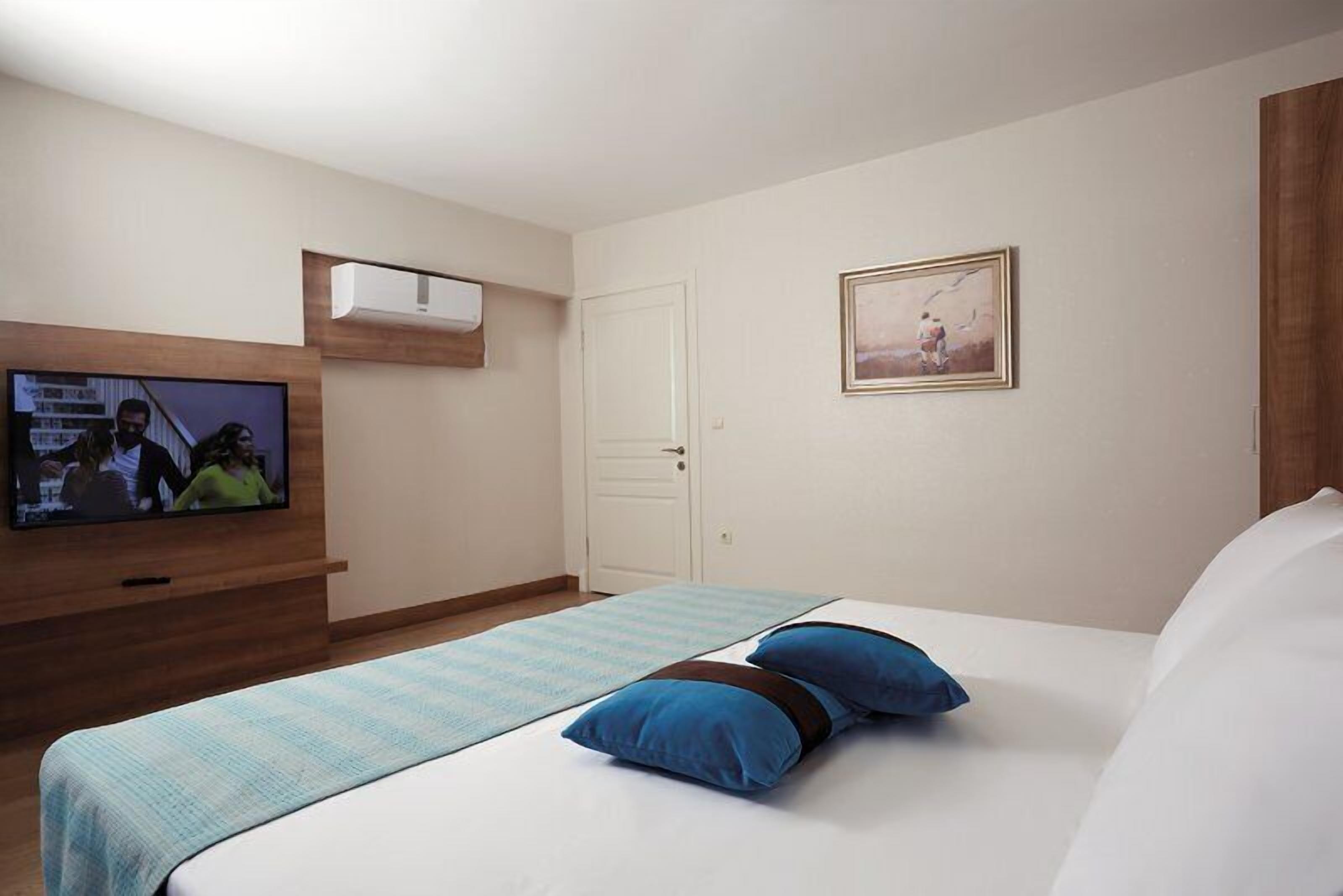 Een hotelkamer met een bed, een aan de muur bevestigde televisie, een deur en een lijst met een afbeelding.