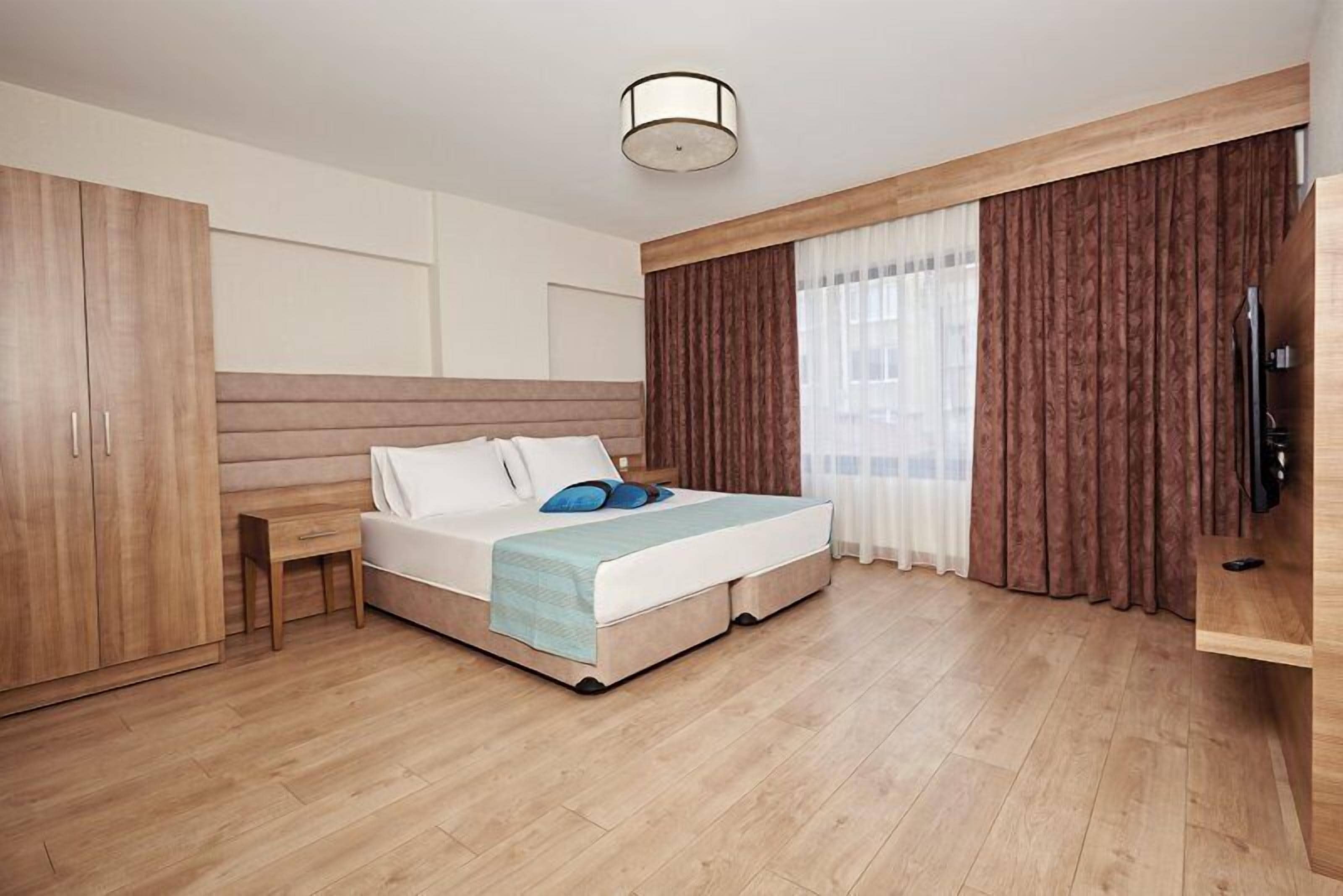 Una habitación de hotel moderna con cama, armario de madera, mesita de noche y televisor.