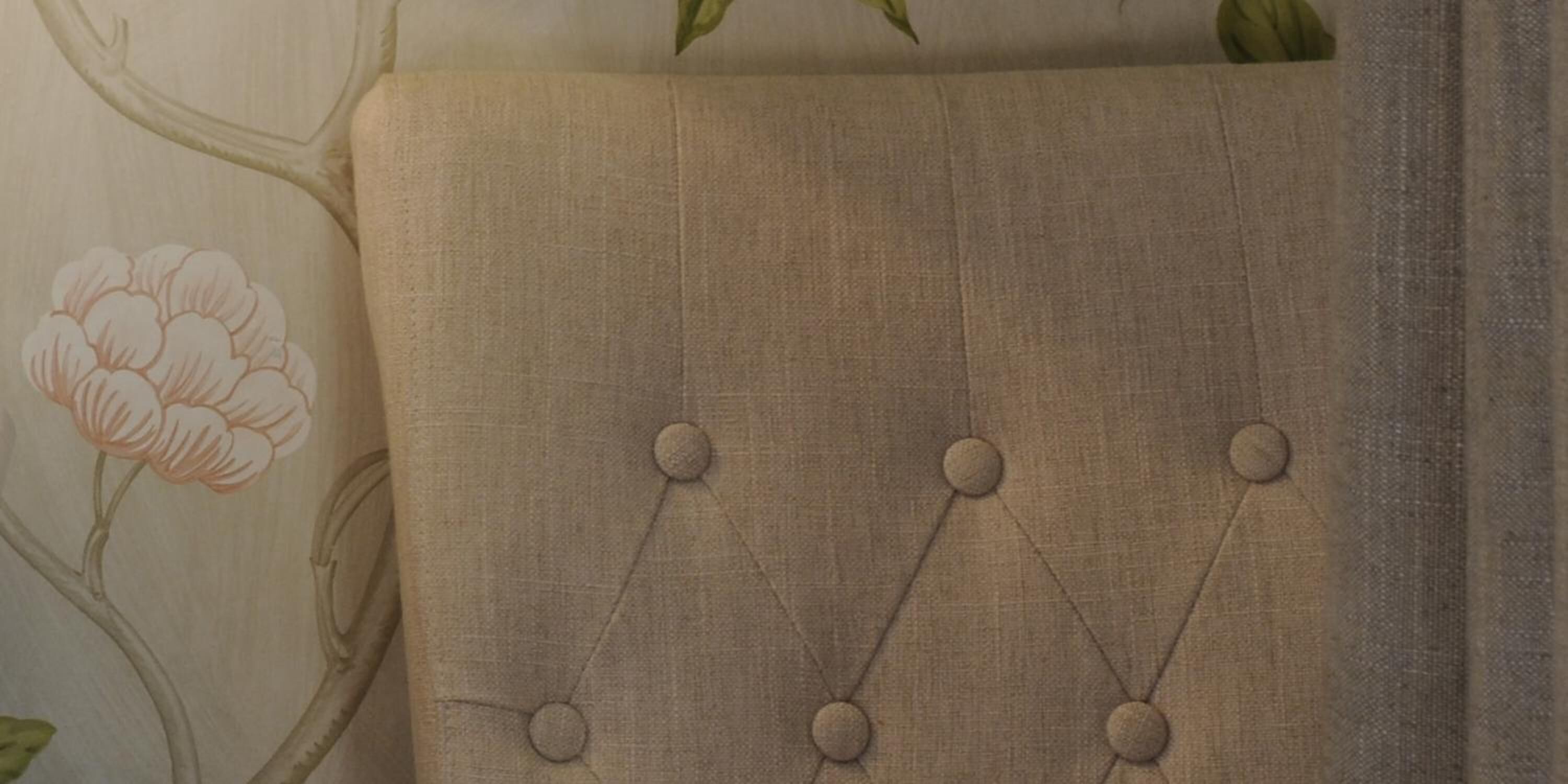 Primer plano de una pared con diseño de papel tapiz floral y un cabecero tapizado.