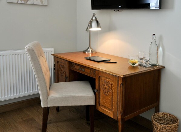 A wooden desk with a lamp, a chair, a tablet, and a bottle.