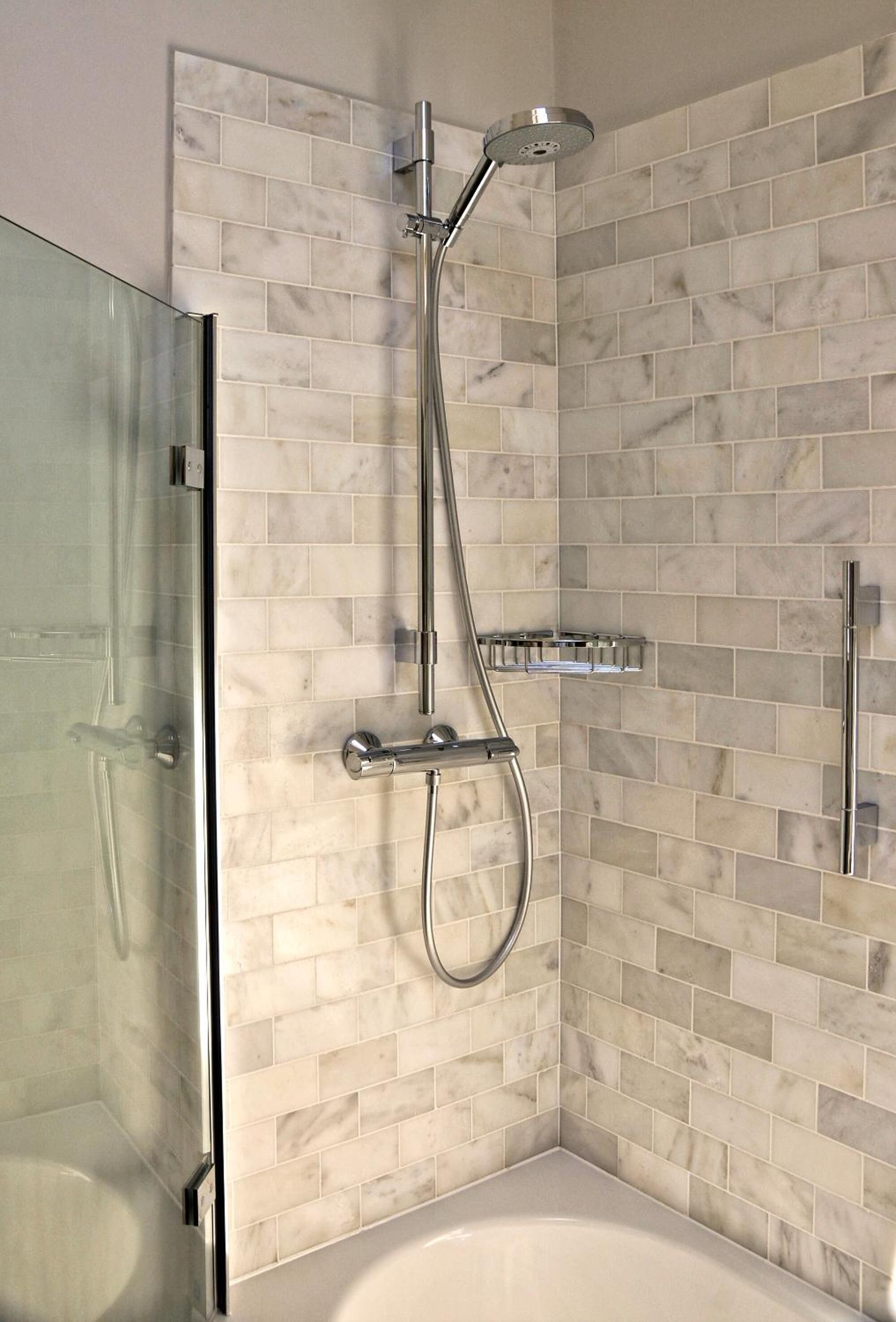 A modern bathroom with a glass shower enclosure, a freestanding bathtub, and a tiled wall with a marble-like pattern.