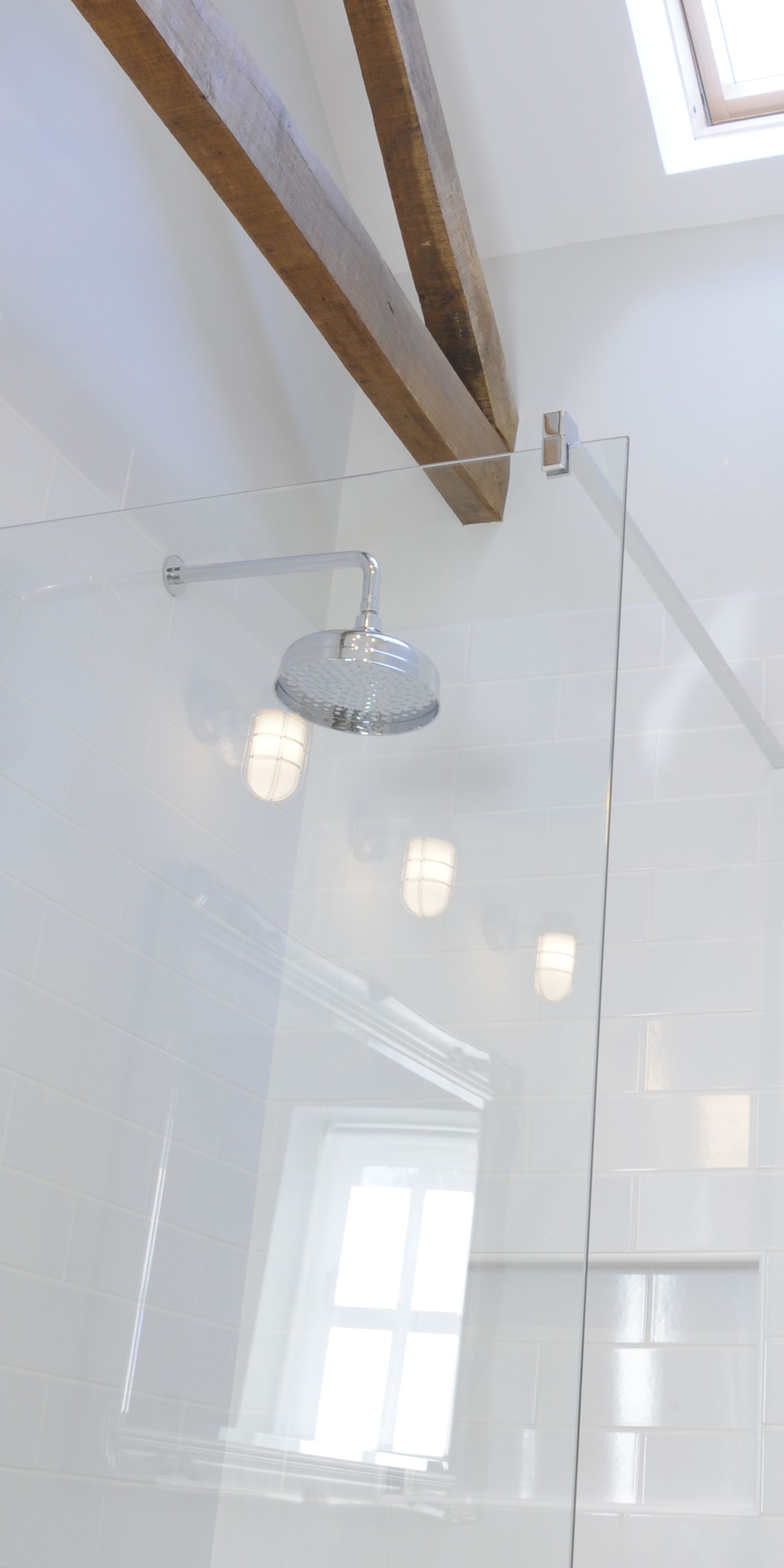 A glass-enclosed shower with a modern design, a wooden ceiling beam, and a view of the outside through a window.