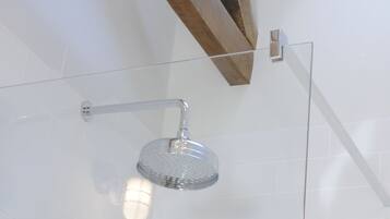 A glass-enclosed shower with a modern design, a wooden ceiling beam, and a view of the outside through a window.