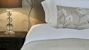 Een net opgemaakt bed met witte lakens en een sierkussen met bloemenborduurwerk.