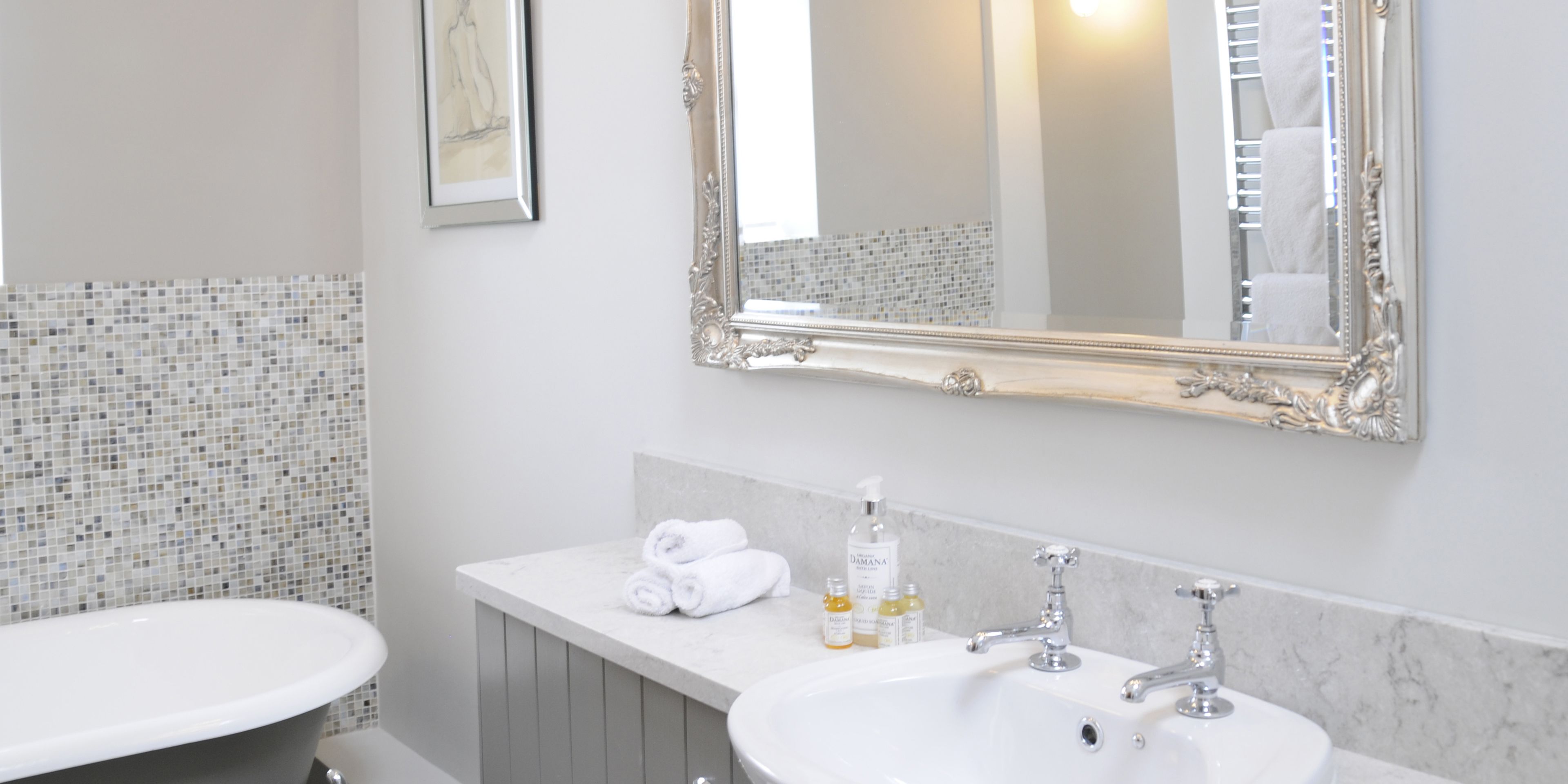 A bathroom with a white bathtub, a white sink, and a large mirror with an ornate frame.